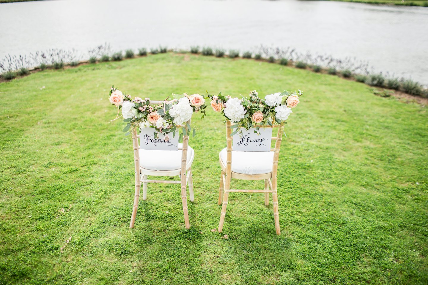 Zwei hölzerne Stühle für eine Hochzeit mit Blumengirlanden auf einer Rasenfläche.